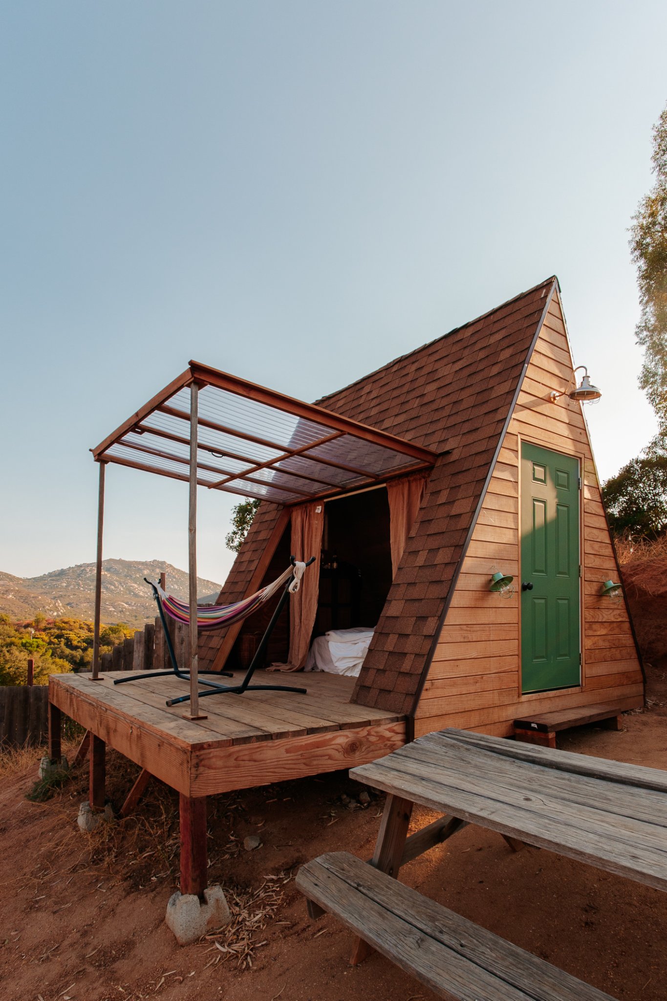 Sativa's wooden deck with a striped hammock under the clear awning, the bed visible inside and hills in the distance